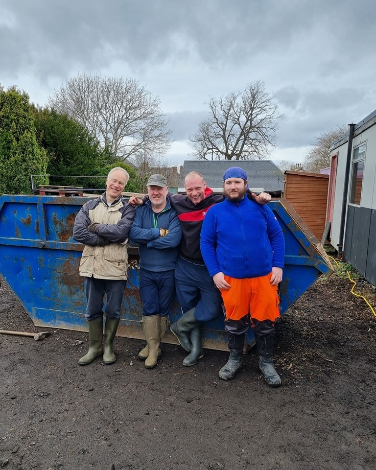 Four men standing in front of a skip looking proud of their volunteering work
