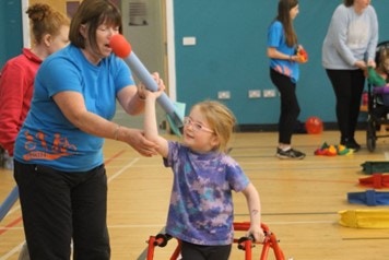 Young girl with mobility support getting ready to throw a practise javalin with the support of a middle age woman 