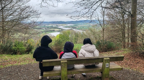 three people sitting on a bench with their backs to the camera looking at a beautiful countryside view