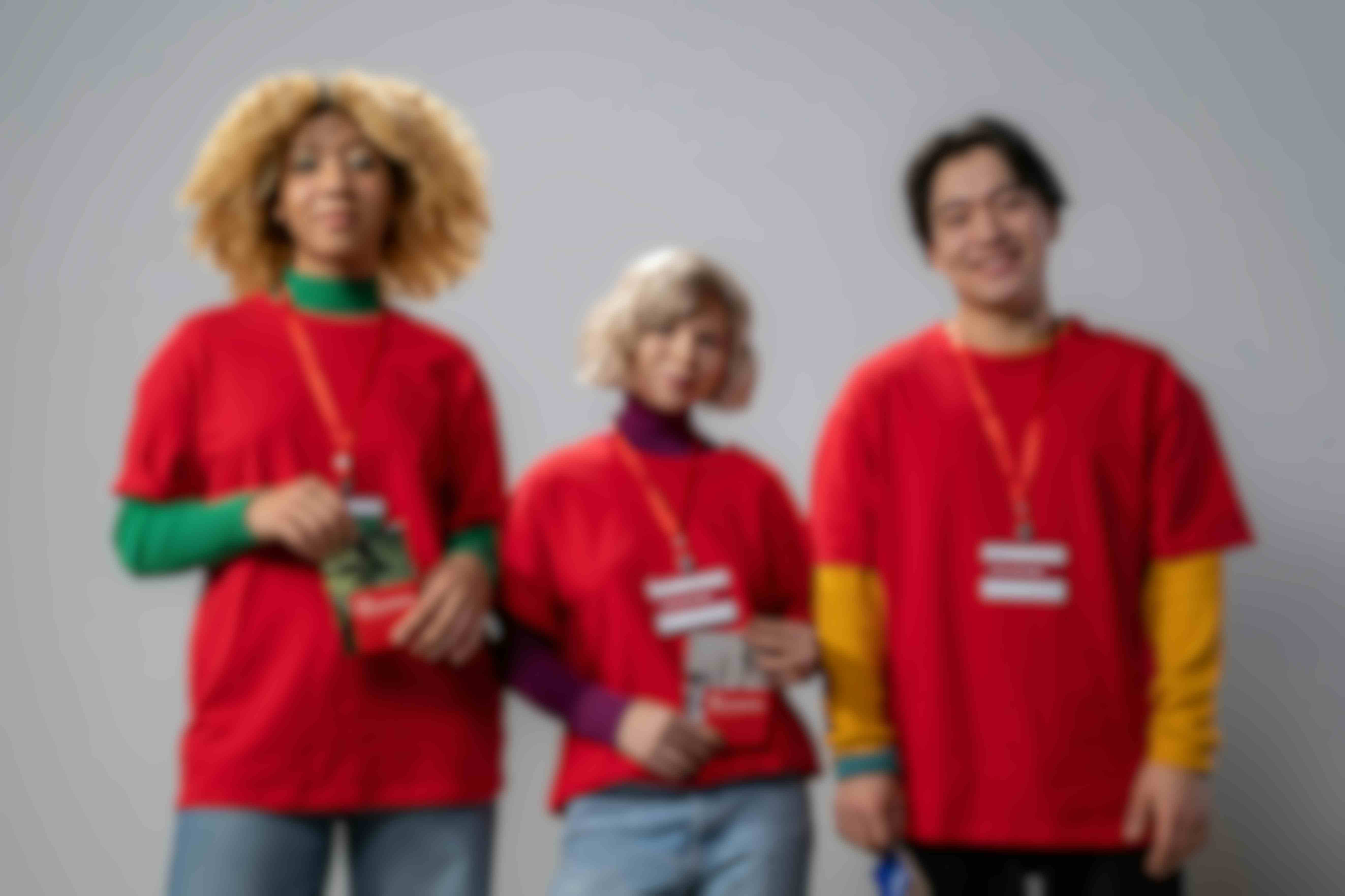 three young people in red tshirts and volunteer lanyards standing and smiling outwards