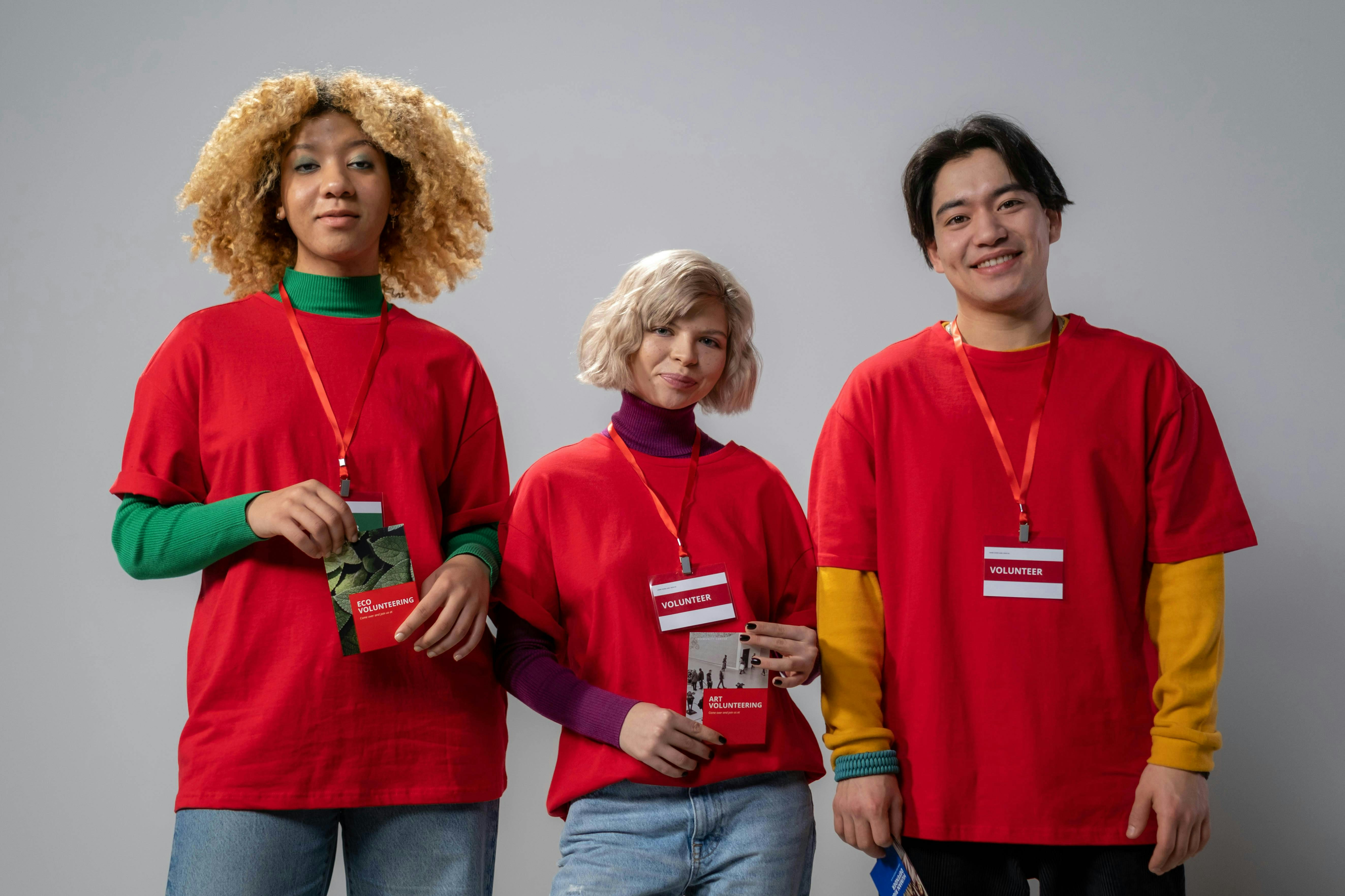 three young people in red tshirts and volunteer lanyards standing and smiling outwards