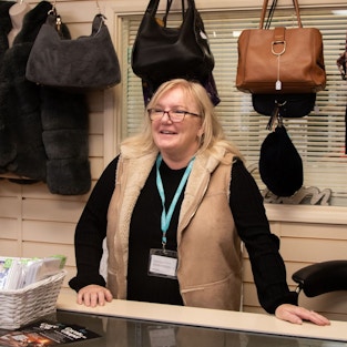Ruth, blonde haired lady with glasses stands at the customer counter in Isabel Hospice shop