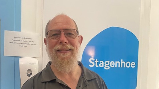 Photo of Jim wearing glasses with a grey beard, smiling at the camera, with the word Stagenhoe in the background