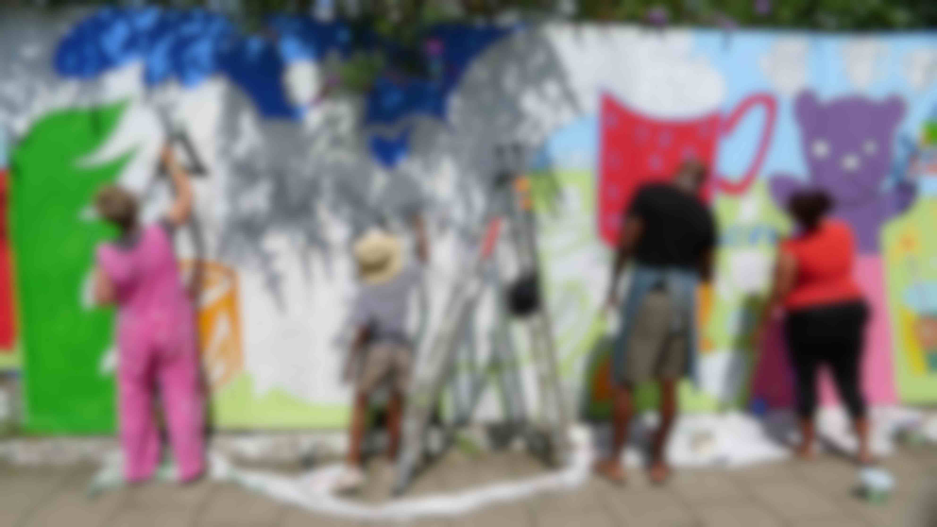 People with their back to the camera painting a mural on a wall