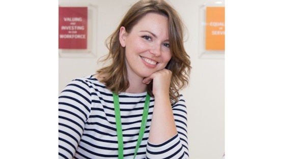 You can see a head and shoulders image of Hannah. She has shoulder length brown hair and is smiling. Hannah is wearing a stripy top and a green lanyard around her neck.